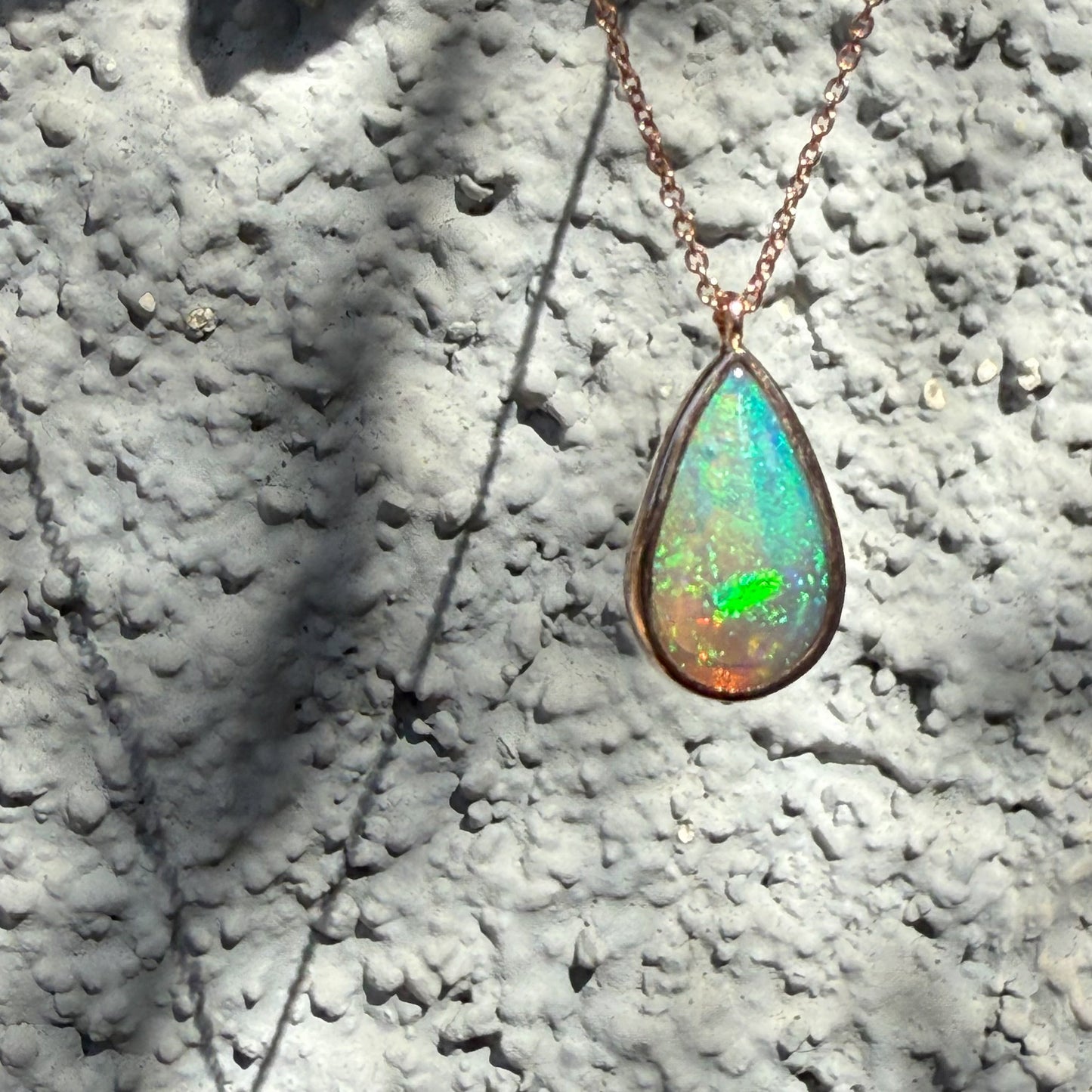 An Australian Opal Necklace by NIXIN Jewelry illuminated by natural light, emphasizing the play-of-color within the pear-shaped crystal opal necklace. The rose gold opal necklace highlights the clarity and color saturation. Unique fine jewelry expertly capturing the elusive beauty of australian opal.