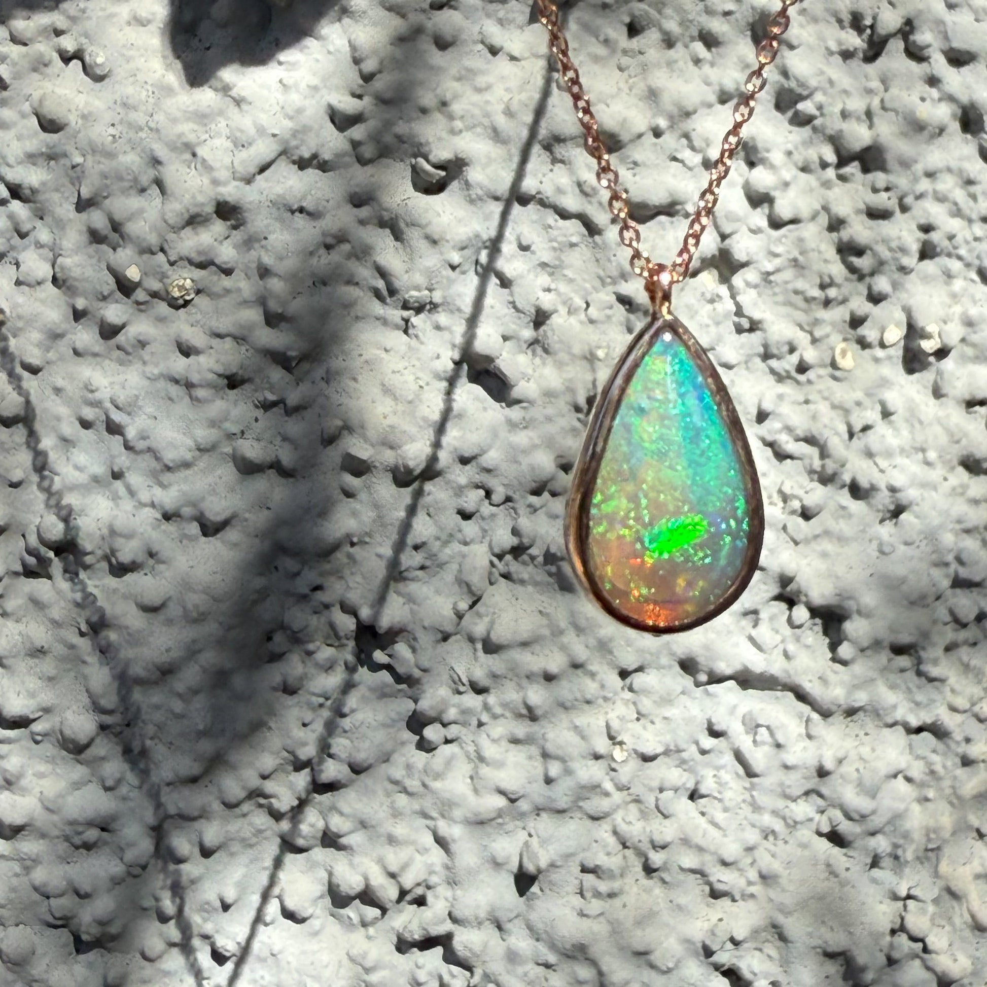 An Australian Opal Necklace by NIXIN Jewelry illuminated by natural light, emphasizing the play-of-color within the pear-shaped crystal opal necklace. The rose gold opal necklace highlights the clarity and color saturation. Unique fine jewelry expertly capturing the elusive beauty of australian opal.