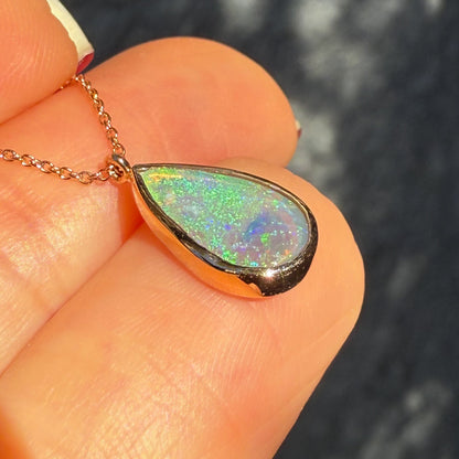 An Australian Opal Necklace by NIXIN Jewelry shown at a profile angle, highlighting the depth and thickness of the cabochon opal pendant. The detailed craftsmanship of the bezel setting and dimensionality of the natural opal attract are visible. This image shows the quality of the unique fine jewelry.