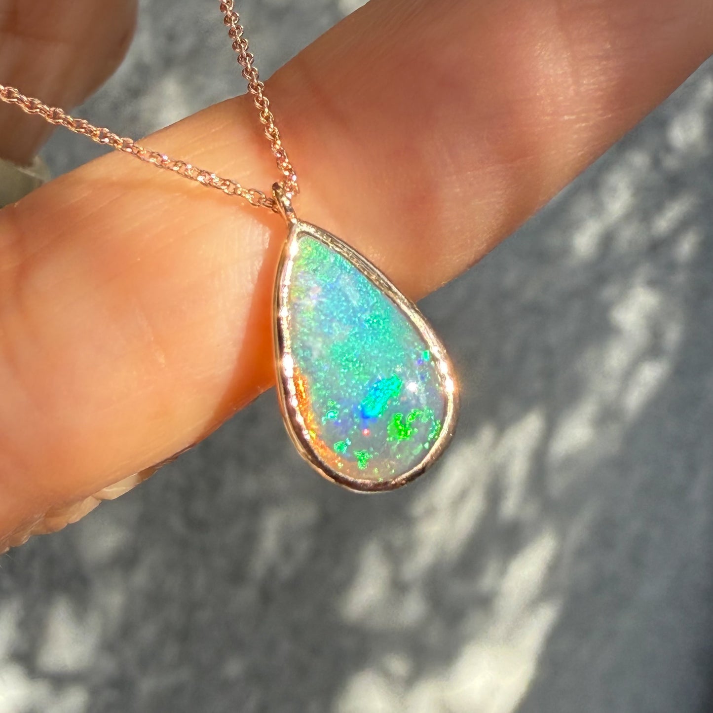 An Australian Opal Necklace by NIXIN Jewelry demonstrating the perfect teardrop shape of the opal stone and a delicate rose gold chain. The bezel setting provides protection and a clean line for this modern opal necklace, which is ideal for clients seeking a rose gold opal necklace.