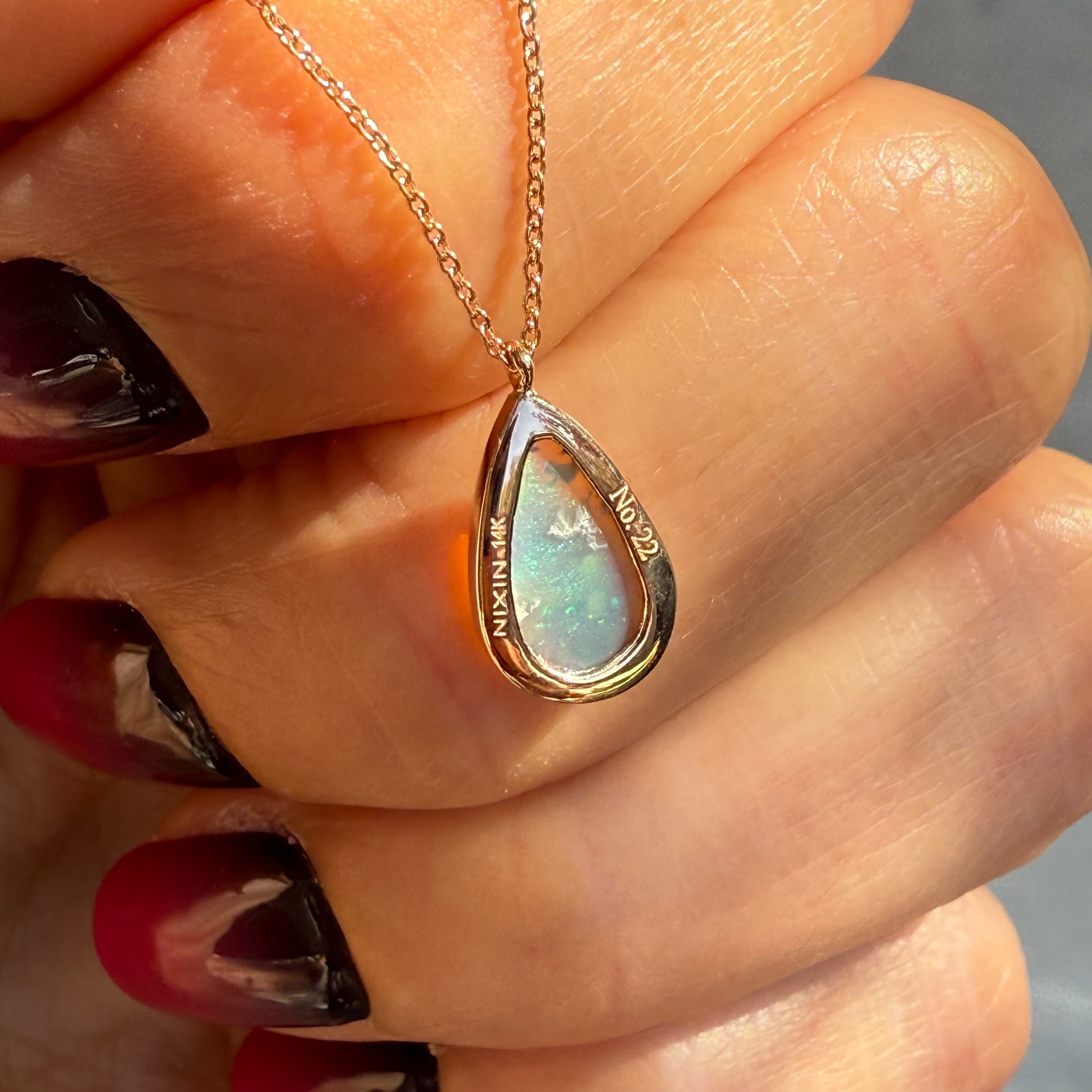 An Australian Opal Necklace by NIXIN Jewelry displaying the authenticity and artisan jewelry hallmark on the back of the pendant. The inscription confirms this piece is NIXIN 14K, Serial Number 22, emphasizing its status as a limited edition unique jewelry design. This shot details the high-quality construction of the opal pendant necklace for buyer confidence.