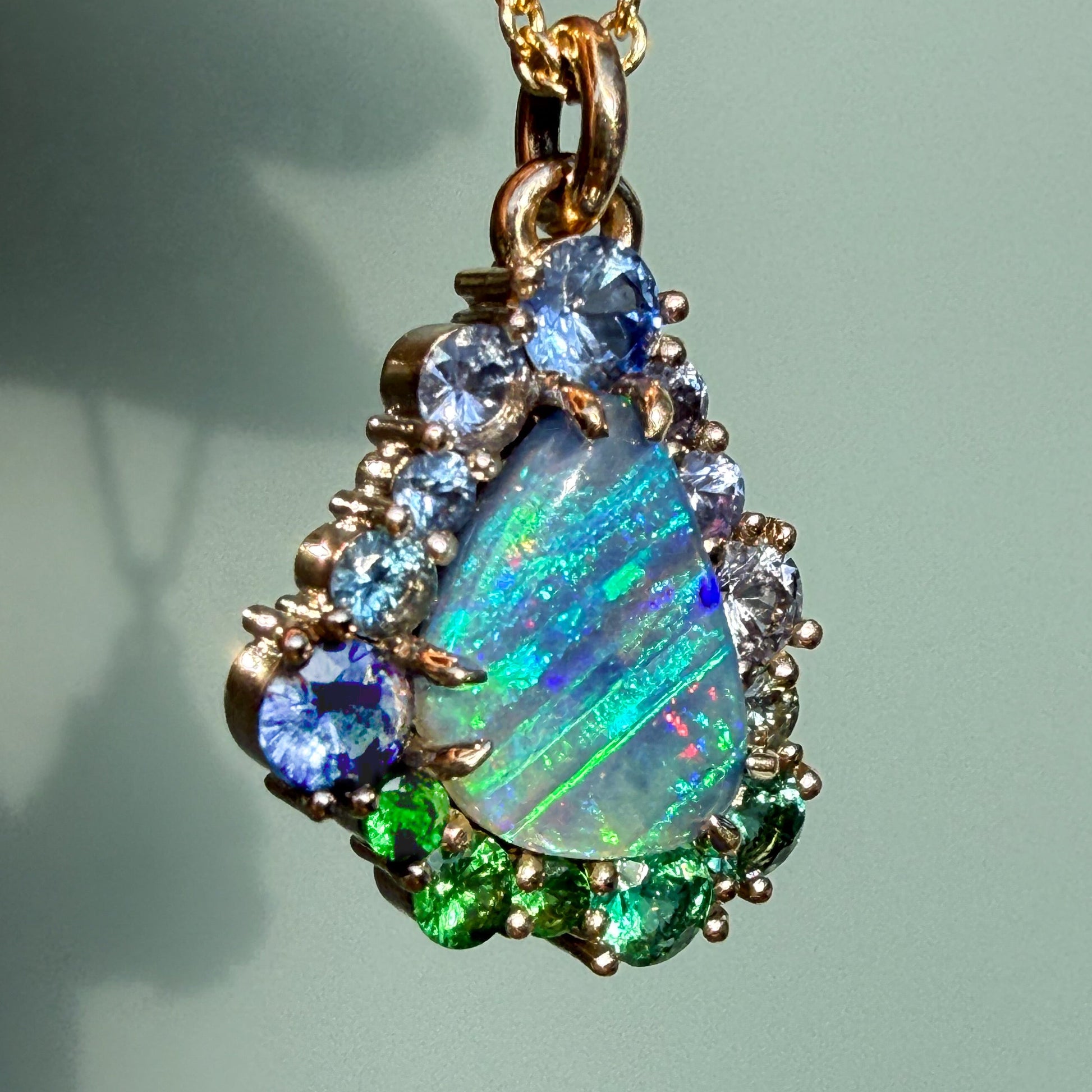 A vibrant front view of an Australian Opal Necklace by NIXIN Jewelry showcases a brilliant blue opal surrounded by a gradient of colorful gemstones. This unique opal jewelry features an ombre jewelry effect transitioning from deep blue sapphires to emeralds and bright green tsavorite garnets.