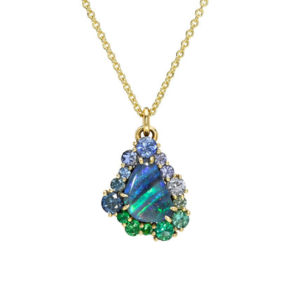 This studio image features an Australian Opal Necklace by NIXIN Jewelry, centered with a vibrant boulder opal with mesmerizing play-of-color. The unique fine jewelry is elevated by an ombre halo of sapphires and emeralds, securely held within prong settings. This women's luxury necklace serves as a piece of jewelry art.