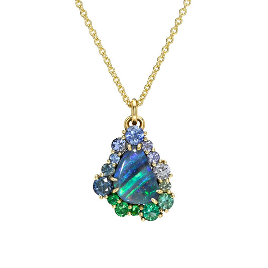 This studio image features an Australian Opal Necklace by NIXIN Jewelry, centered with a vibrant boulder opal with mesmerizing play-of-color. The unique fine jewelry is elevated by an ombre halo of sapphires and emeralds, securely held within prong settings. This women's luxury necklace serves as a piece of jewelry art.