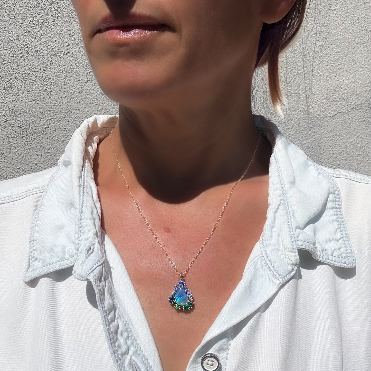 This lifestyle shot features an Australian Opal Necklace by NIXIN Jewelry, demonstrating the scale of the opal pendant when worn. The women's luxury necklace showcases a blue opal and a sapphire halo that creates a striking ombre jewelry effect. This rare jewelry highlights the beauty of a natural opal set in polish gold, making it a masterpiece of unique fine jewelry.