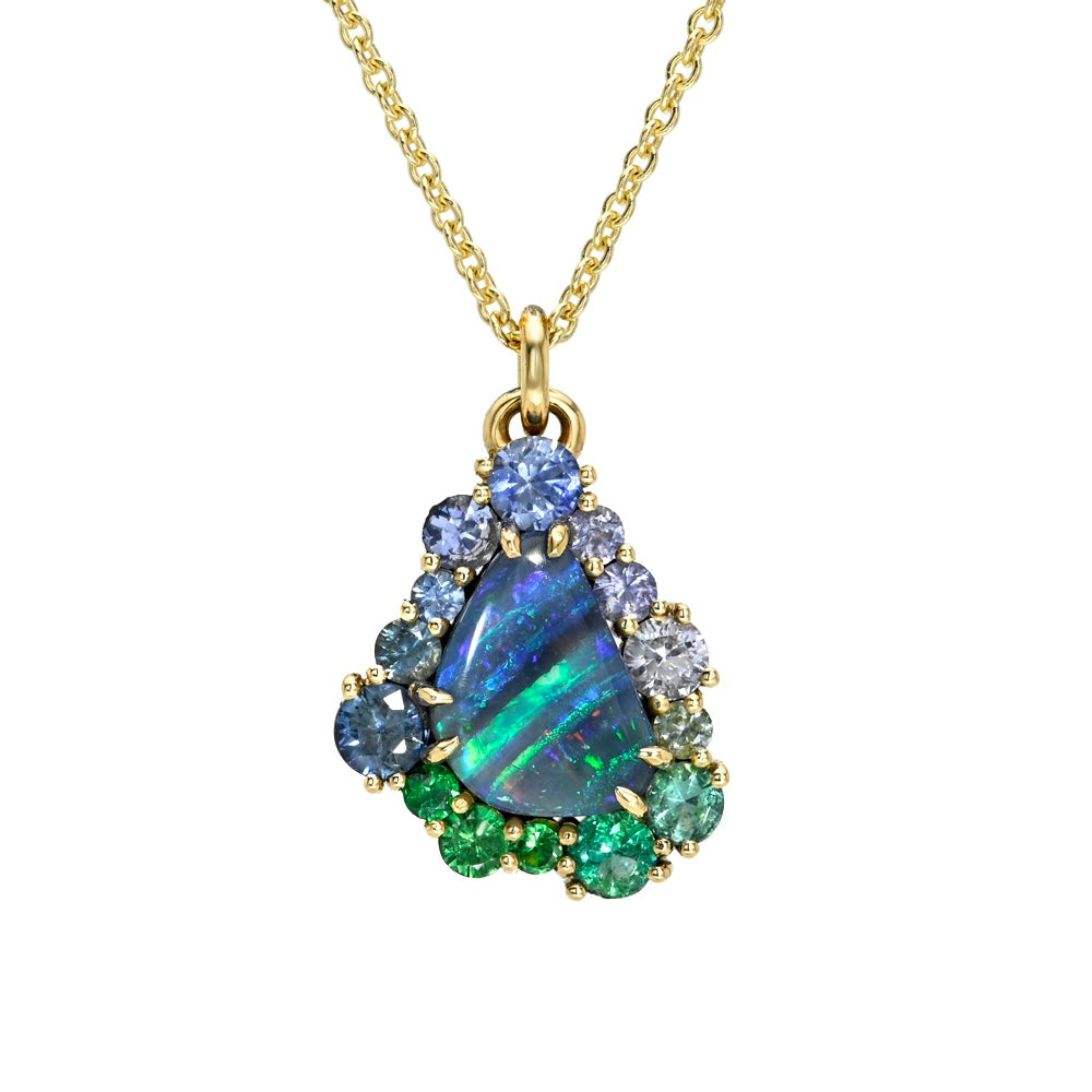 This studio image features an Australian Opal Necklace by NIXIN Jewelry, centered with a vibrant boulder opal with mesmerizing play-of-color. The unique fine jewelry is elevated by an ombre halo of sapphires and emeralds, securely held within prong settings. This women's luxury necklace serves as a piece of jewelry art.
