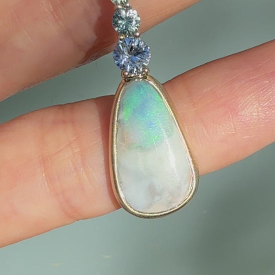 An Australian Opal Pendant by NIXIN Jewelry video capturing the exceptional light and color play of the natural blue opal set in a matte gold bezel setting. The video highlights the shimmering ombré sapphires and the quality of this unique opal necklace, making it perfect for clients searching for women's luxury necklace or rare jewelry. This is jewelry art designed to display the opal's full brilliance.
