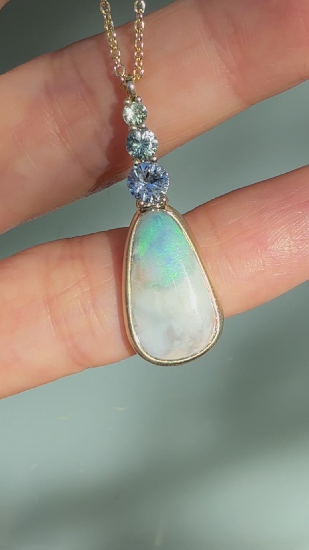 An Australian Opal Pendant by NIXIN Jewelry video capturing the exceptional light and color play of the natural blue opal set in a matte gold bezel setting. The video highlights the shimmering ombré sapphires and the quality of this unique opal necklace, making it perfect for clients searching for women's luxury necklace or rare jewelry. This is jewelry art designed to display the opal's full brilliance.