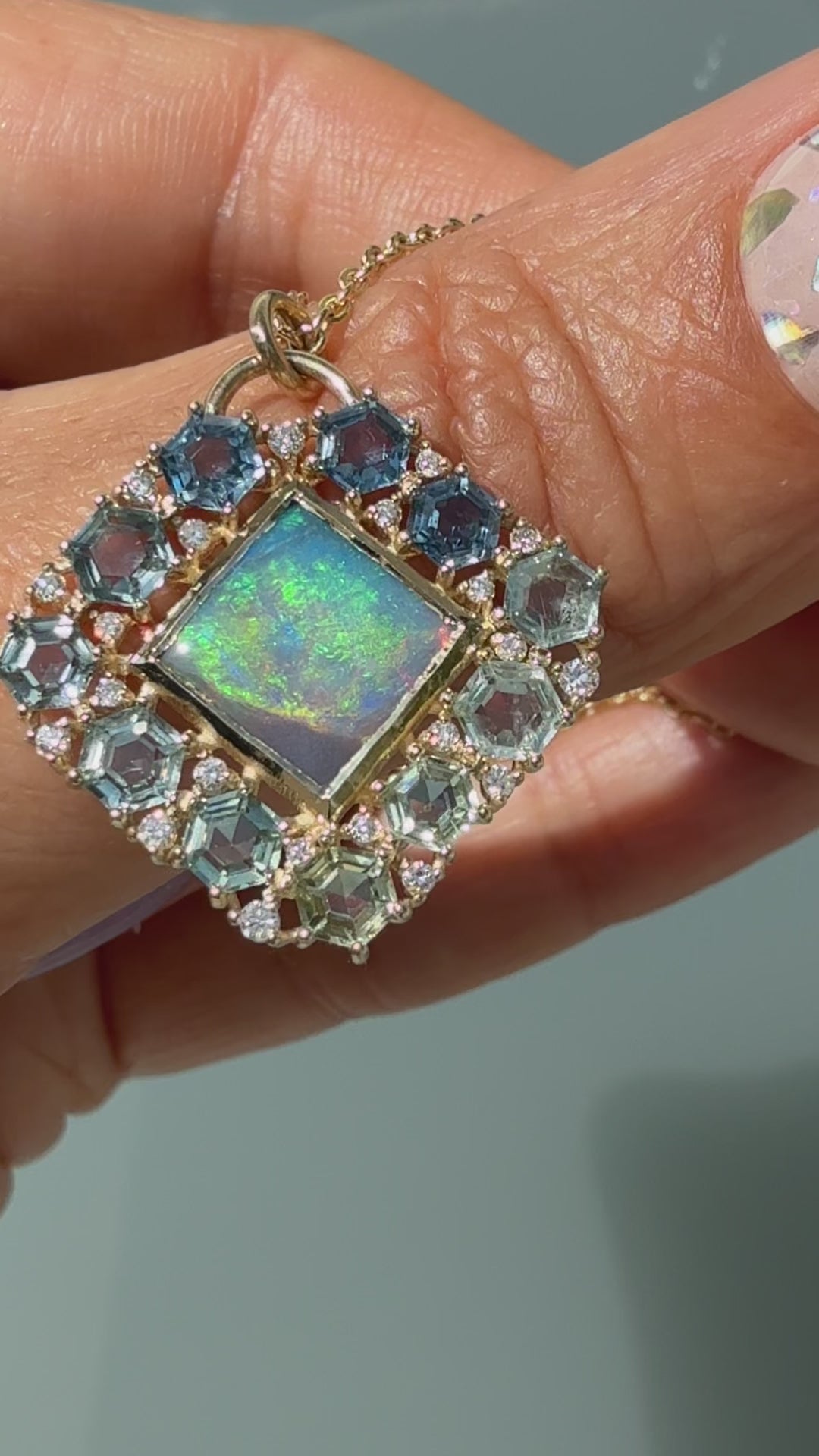 A video demonstration highlights the dynamic color shifts of an Australian Opal Pendant by NIXIN Jewelry as it moves through the light. The luxury black opal necklace features a rare lightning ridge opal in a gold bezel setting, bordered by an ombre halo of hexagon-cut montana sapphires and prong-set diamonds. The footage also turns to capture the reverse side, showcasing a structural honeycomb latticework that elevates this piece of unique fine jewelry into a work of wearable jewelry art.