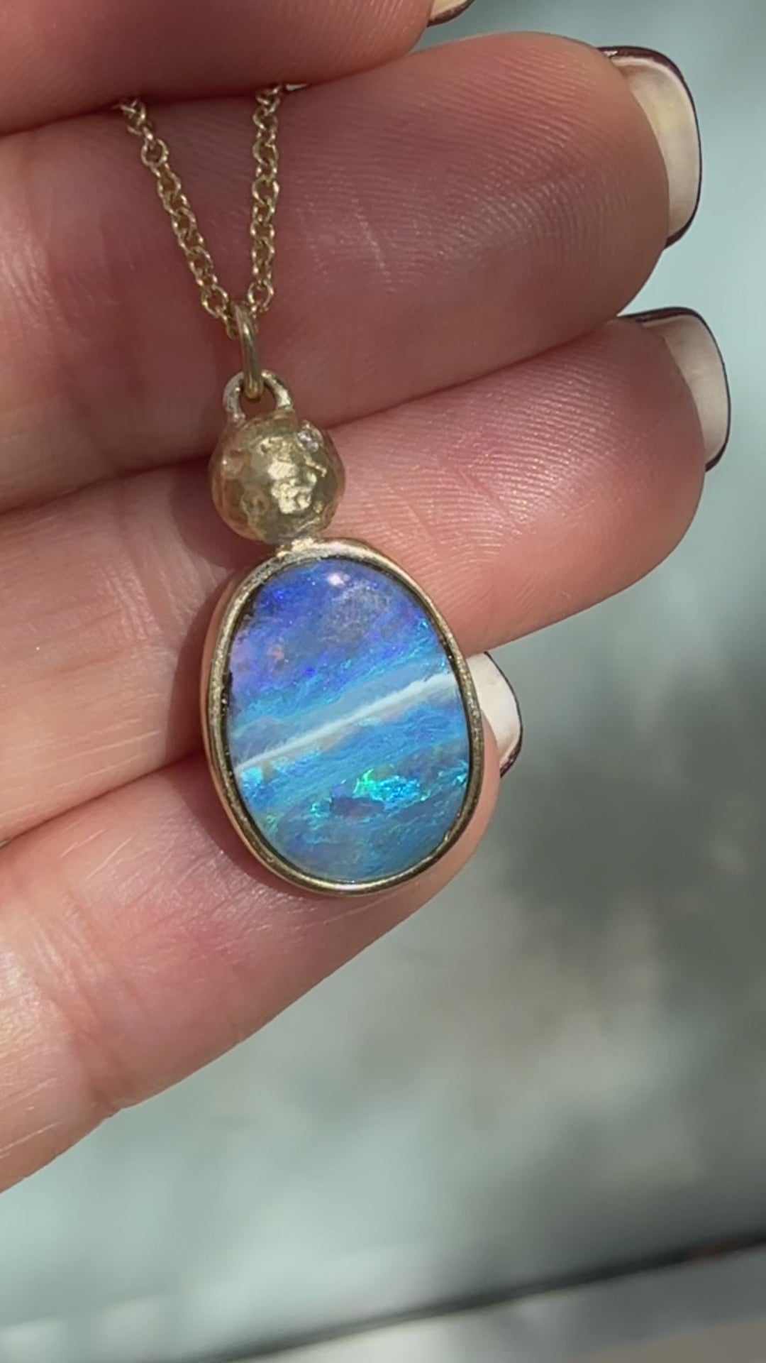 An Australian Opal Necklace by NIXIN Jewelry is showcased in this video to display the shifting play of color across the natural blue opal. This boulder opal necklace features a polish gold bezel setting and a handcrafted solid gold moon, exemplifying the artistry of unique jewelry. A luxury necklace for those seeking high jewelry.