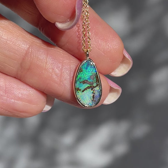 Video of an Australian Opal Necklace by NIXIN Jewelry held in the sunlight to show its colors. The opal is blue and green, set in 14k gold and hangs from a link chain.