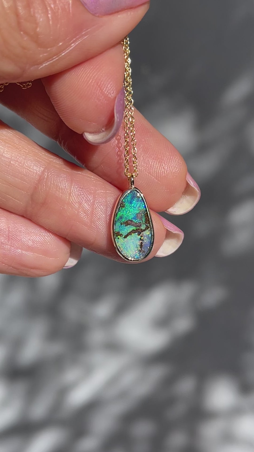 Video of an Australian Opal Necklace by NIXIN Jewelry held in the sunlight to show its colors. The opal is blue and green, set in 14k gold and hangs from a link chain.