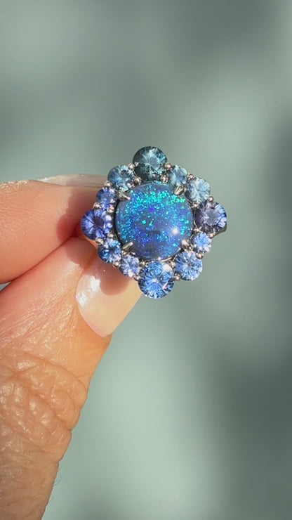 An Australian Opal Ring by NIXIN Jewelry. This video captures the close-up rotation of the magnificent black opal and sapphire opal ring cluster in its prong setting. The movement highlights the depth of color and the brilliance of this luxury ring, showcasing the meticulous craftsmanship of this unique jewelry piece.