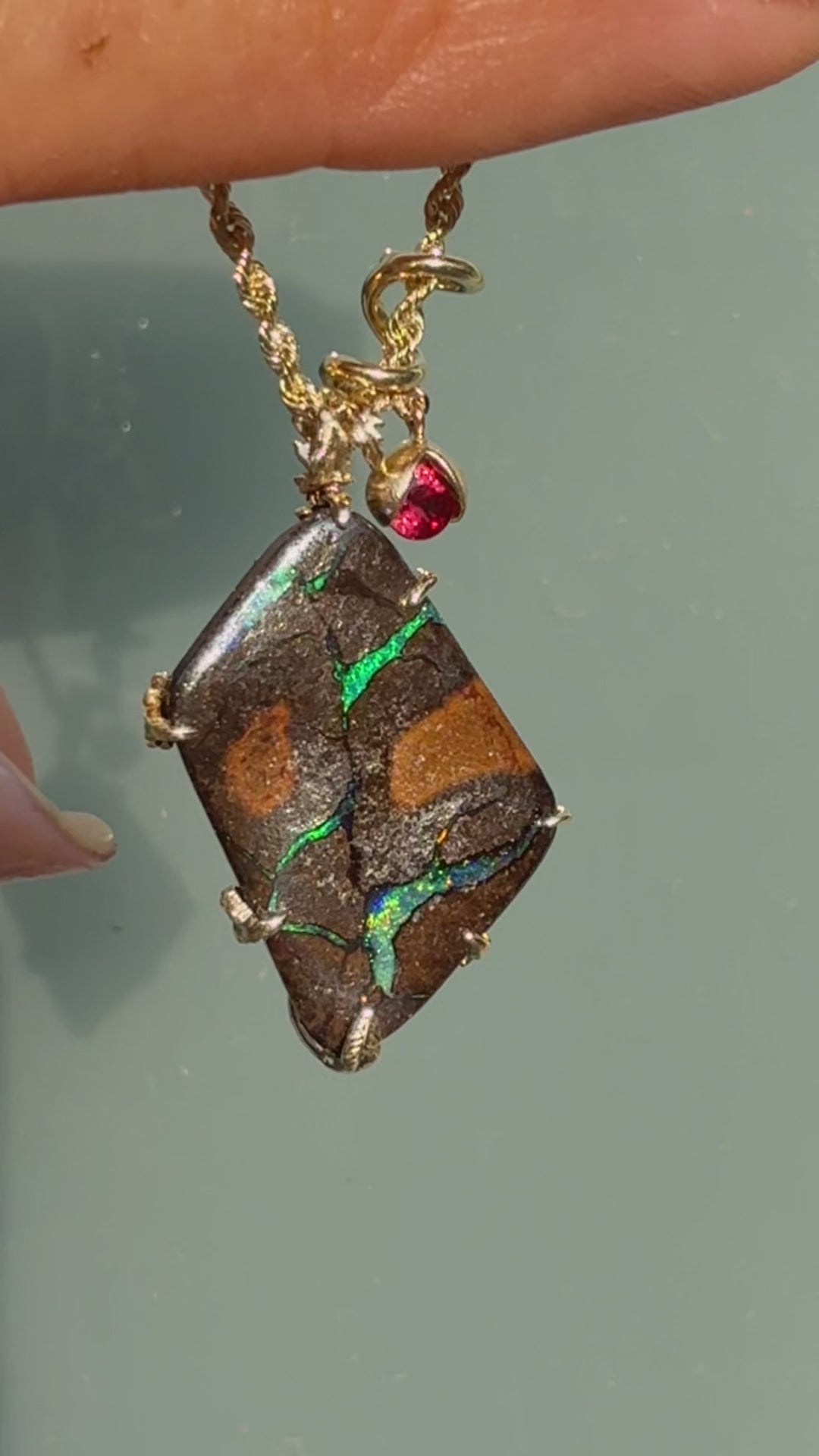 An Australian Opal Pendant by NIXIN Jewelry is shown in motion to reveal the breathtaking craftsmanship and slivers of play of color, shifting from emerald green to cobalt and red. This video highlights the three-dimensional 14k gold poppy design and shimmering red rubies as they catch the light, showcasing the exquisite detail of this jewelry art. It provides a dynamic look at a unique fine jewelry masterpiece, demonstrating the fluid elegance and luxury of a high-end boulder opal necklace.