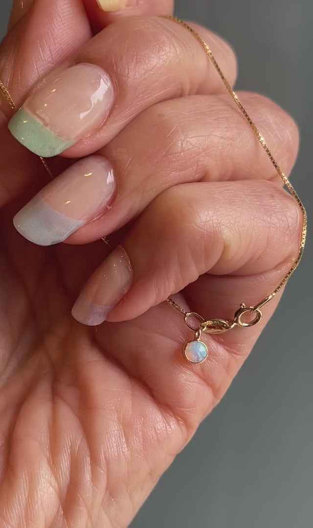 Video of an Australian Opal Bracelet by NIXIN Jewelry. Held to show the front and back of the opal charm, its bezel setting and the gold box chain of the simple bracelet.