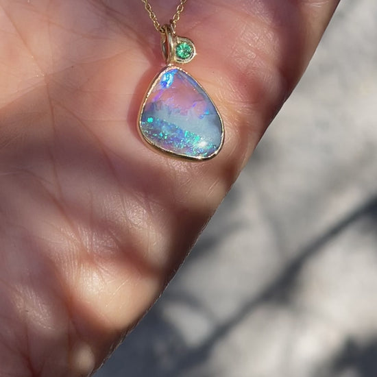 Video of an Australian Opal Necklace by  NIXIN Jewelry in yellow gold with a black opal in a bezel setting and a small emerald.