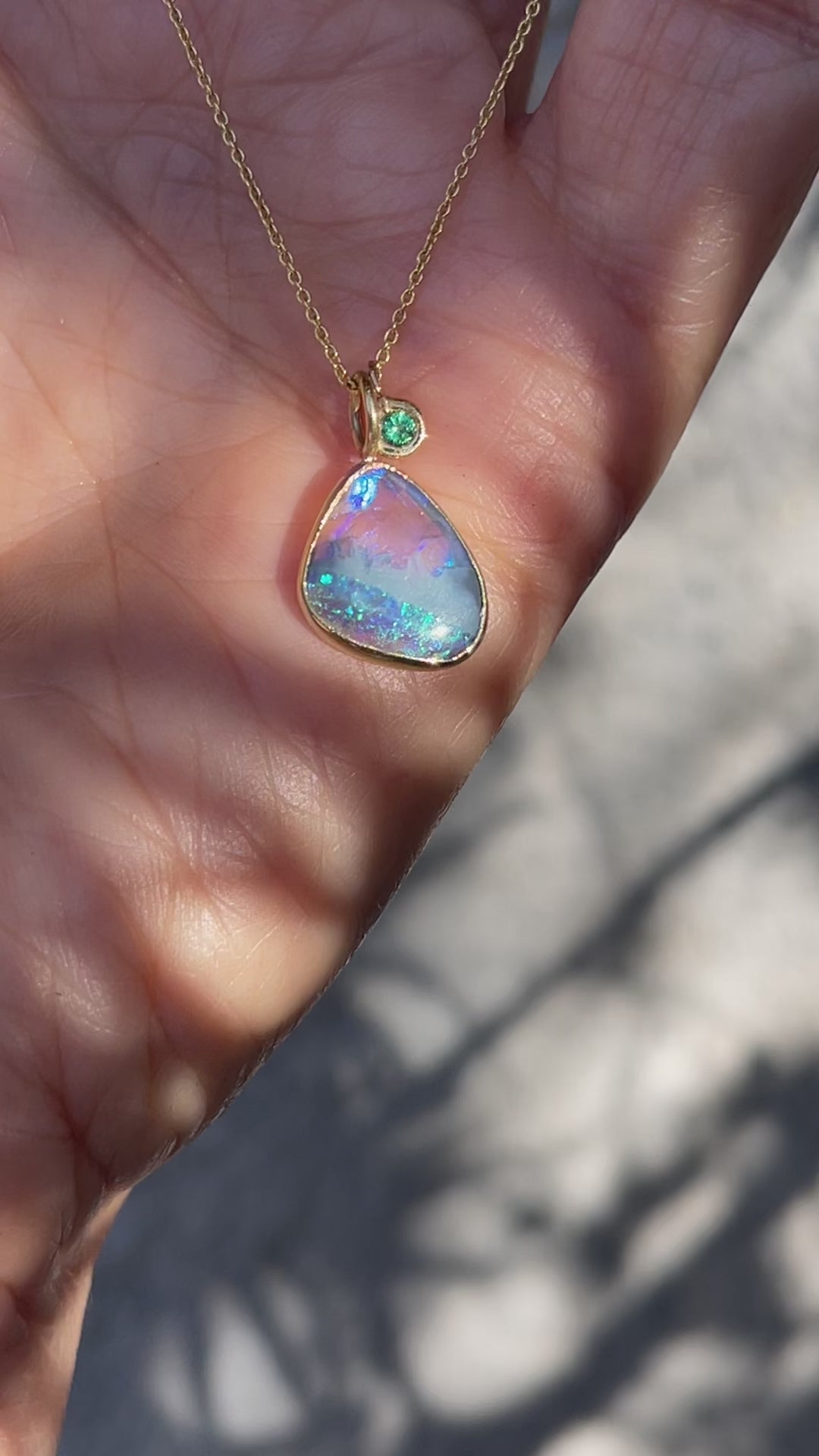 Video of an Australian Opal Necklace by  NIXIN Jewelry in yellow gold with a black opal in a bezel setting and a small emerald.