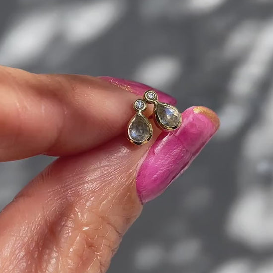 A video of Moonstone Earrings by NIXIN Jewelry held in the sunlight. The dainty studs are made with blue moonstone and tiny diamonds.