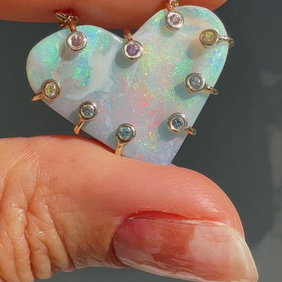 An Australian Opal Necklace by NIXIN Jewelry video capturing the play-of-color across the heart-shaped opal pendant in direct sunlight. The movement demonstrates the lightning ridge opal shifting from green and blue to red and pink flashes. This highly desirable unique opal jewelry piece is optimized for the luxury market.