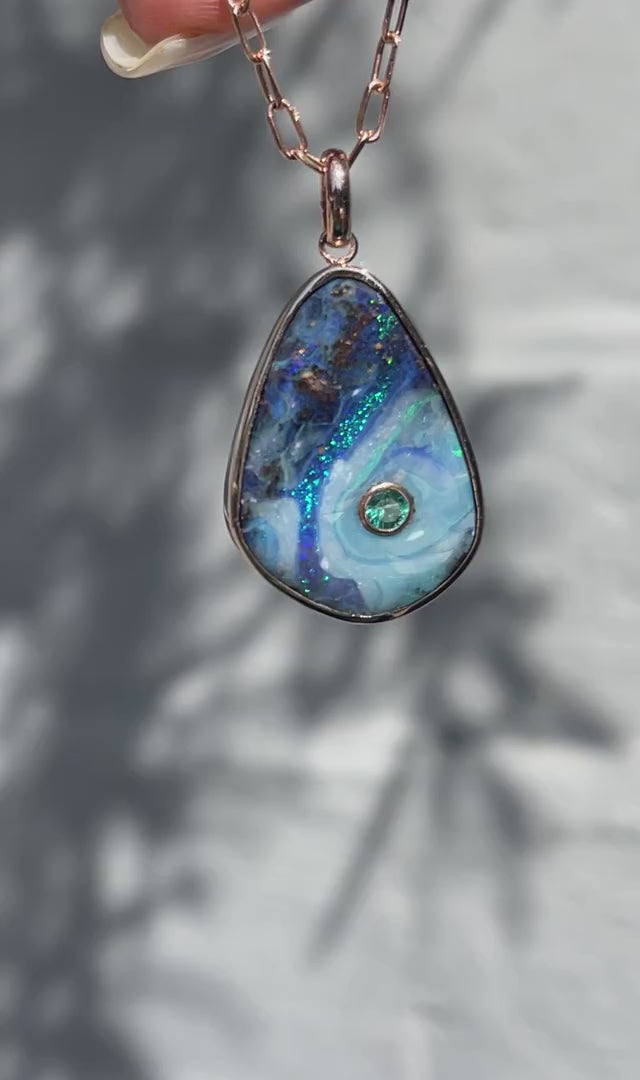 Video of an Australian Opal Necklace by NIXIN Jewelry moving in the sunlight. It highlights the color pattern of the blue opal and the intensity of the emerald in the pendant.