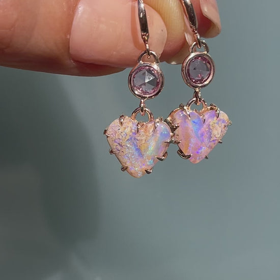 Video of a pair of Australian Opal Earrings by NIXIN Jewelry held in the sunlight. The heart earrings have purple opals and sapphires.