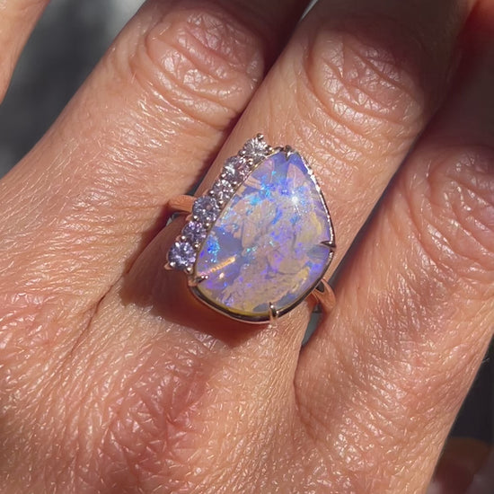 Video of an Australian Opal Ring by NIXIN Jewelry modeled on a hand. The rose gold opal ring has a Crystal opal and a pink and purple sapphire border.