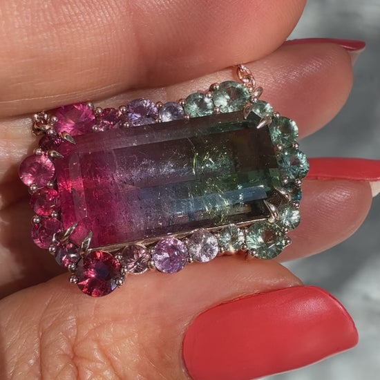 Video of the Empress Imbued Tourmaline Necklace by NIXIN Jewelry rotating in hand outdoors, showcasing the ruby and sapphire halo around the tri-color tourmaline and the rose gold chain in natural light.
