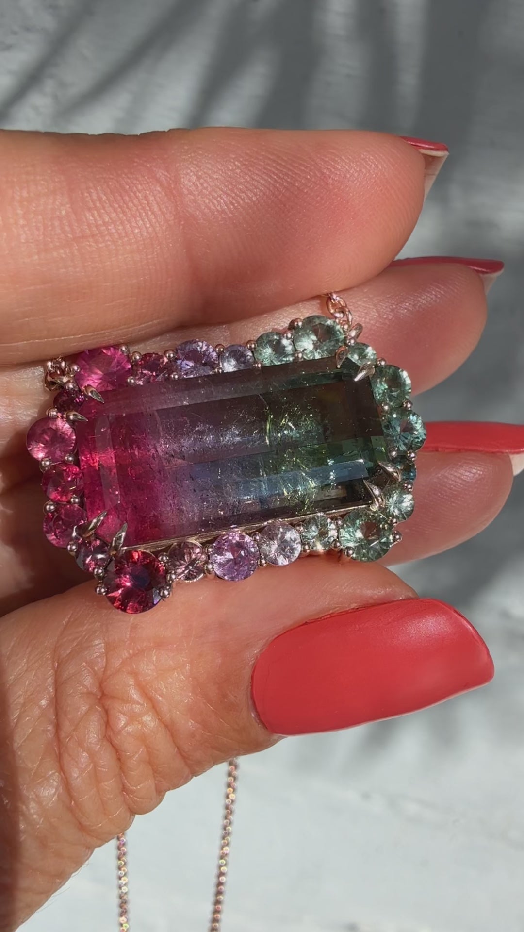 Video of the Empress Imbued Tourmaline Necklace by NIXIN Jewelry rotating in hand outdoors, showcasing the ruby and sapphire halo around the tri-color tourmaline and the rose gold chain in natural light.