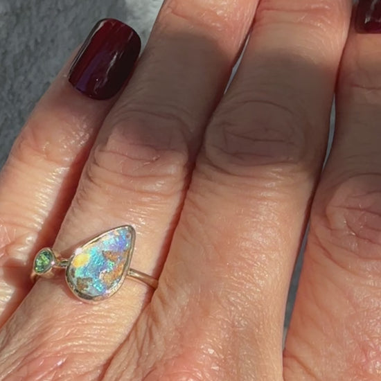 This Australian opal ring by NIXIN Jewelry is showcased in a video that captures the shifting play-of-color across its vibrant surface. As the hand moves, the pear shaped opal reveals deep flashes of lavender and electric blue, while the brilliant emerald flickers like a vivid green beacon. This high-definition look at the unique fine jewelry highlights the secure bezel setting and the modern design, making it an exquisite example of rare opal jewelry.