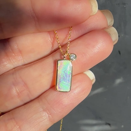 A video showing an Australian Opal Necklace by NIXIN Jewelry in sunlight. The video captures the play-of-color within the crystal opal stone as it moves. The footage highlights the detailed gold setting, the bezel-set diamond, and the craftsmanship of this luxurious opal pendant.