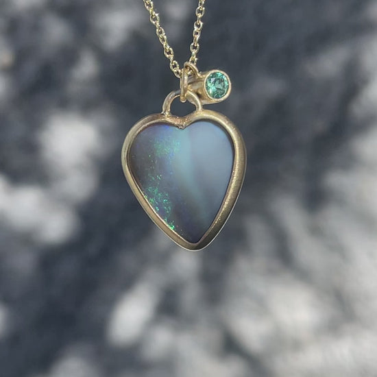 Video of an Australian Opal Necklace by NIXIN Jewelry with a black opal pendant, an emerald and a blue sapphire charm.