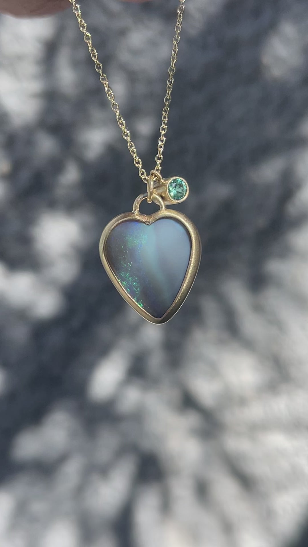 Video of an Australian Opal Necklace by NIXIN Jewelry with a black opal pendant, an emerald and a blue sapphire charm.