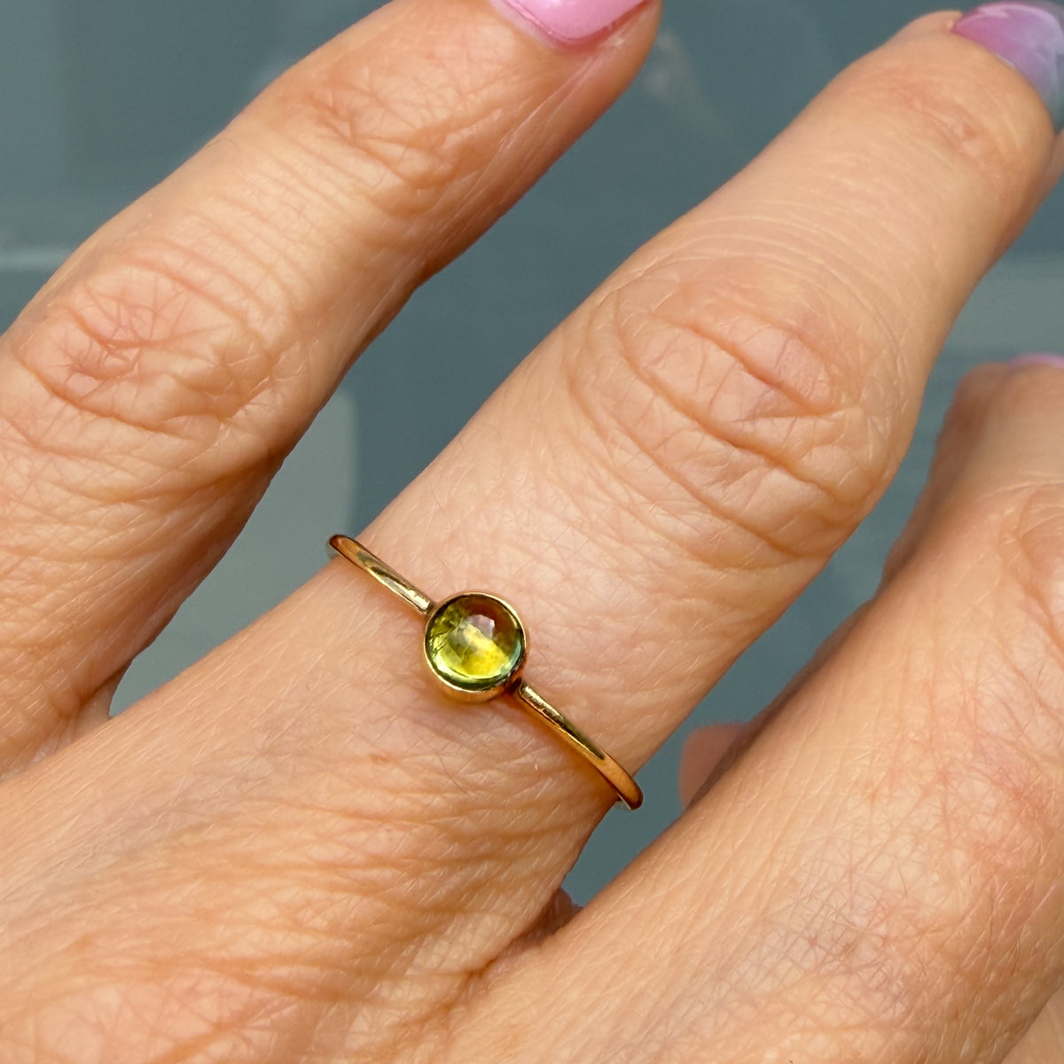 Lucky Green Tourmaline Ring worn alone, a single pale chartreuse tourmaline cabochon in a 14k gold bezel on a slim band.