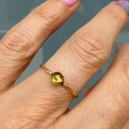 Lucky Green Tourmaline Ring worn alone, a single pale chartreuse tourmaline cabochon in a 14k gold bezel on a slim band.