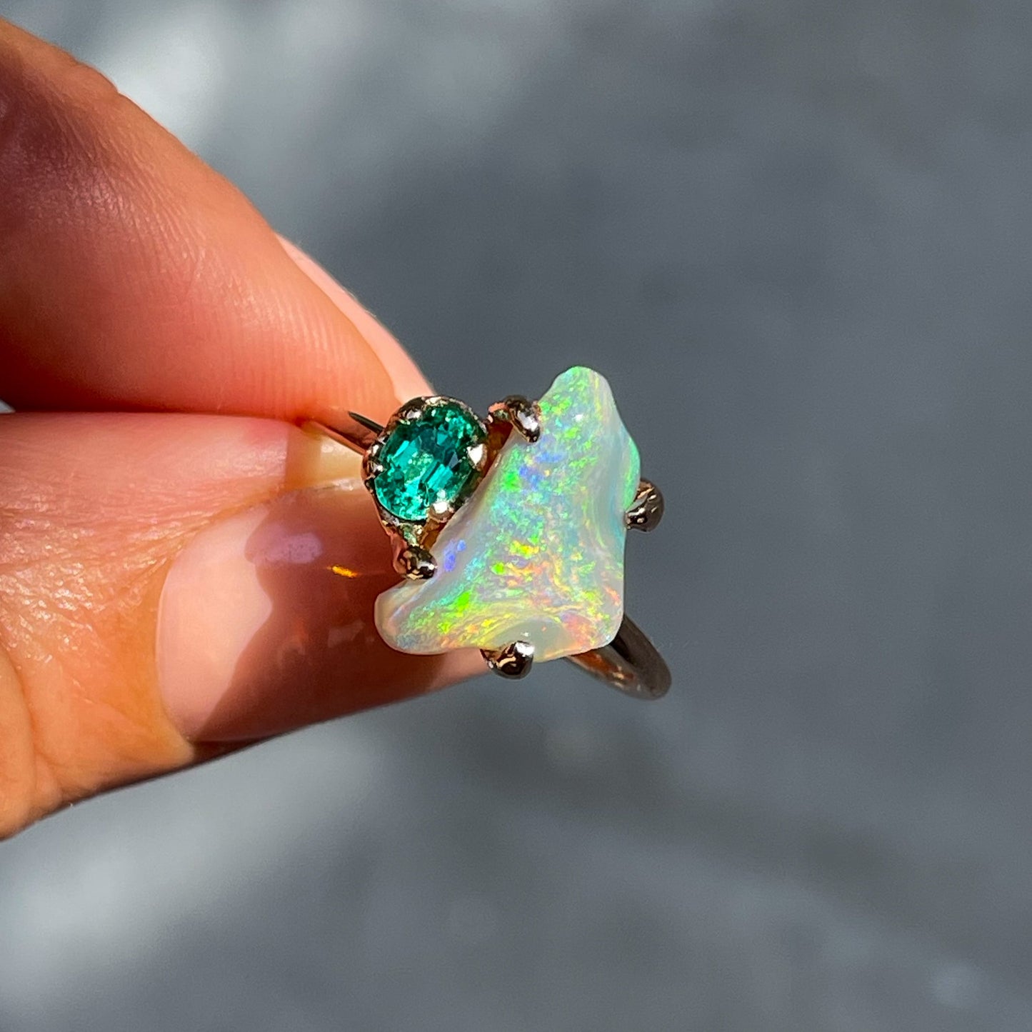 An Opal and Emerald Ring by NIXIN Jewelry held in direct sunlight. The emerald and black opal are secured by prong setting.