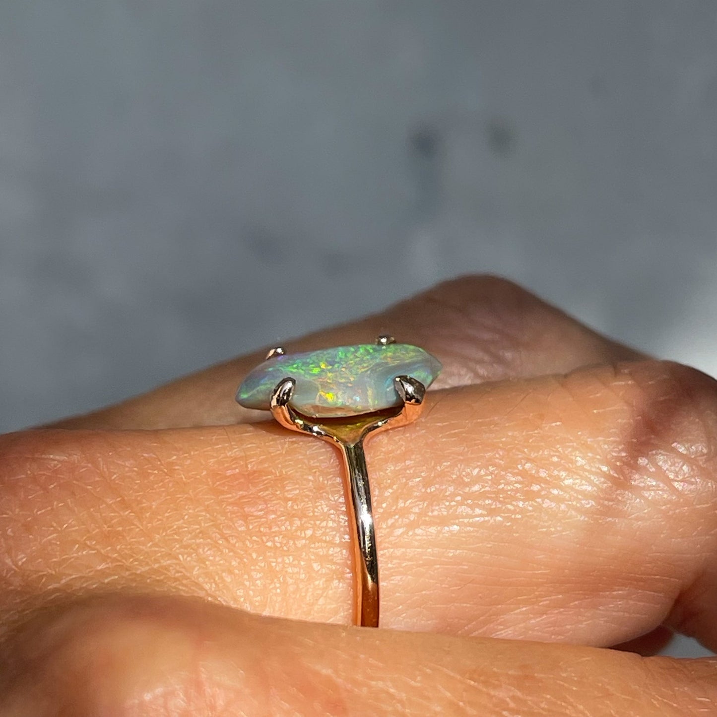 A profile shot of an Opal and Emerald Ring by NIXIN Jewelry modeled on the finger. The image shows the height of the rose gold opal ring.