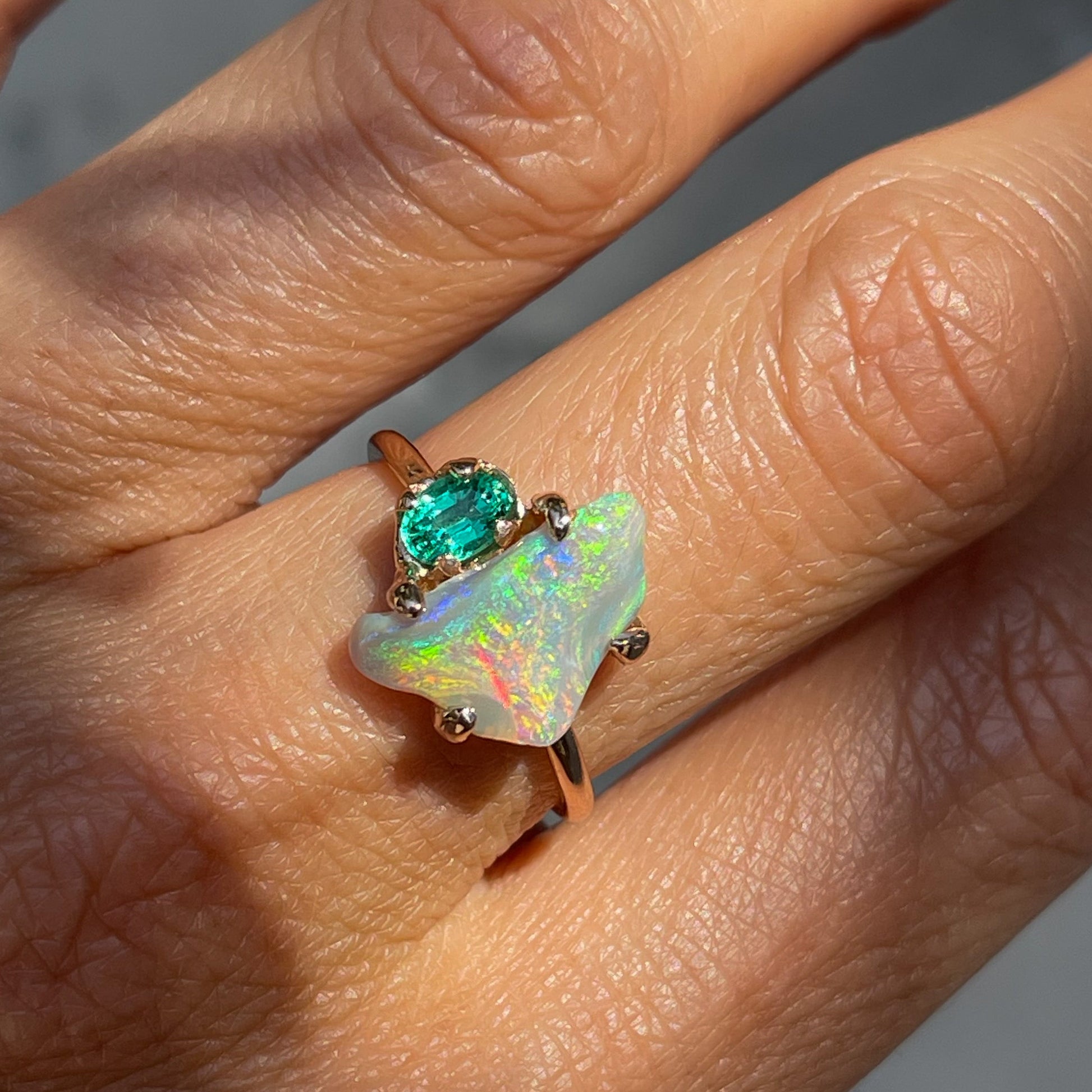 An Opal and Emerald Ring by NIXIN Jewelry modeled on a hand. The opal ring is among the rare jewelry offerings on NIXINjewelry.com.