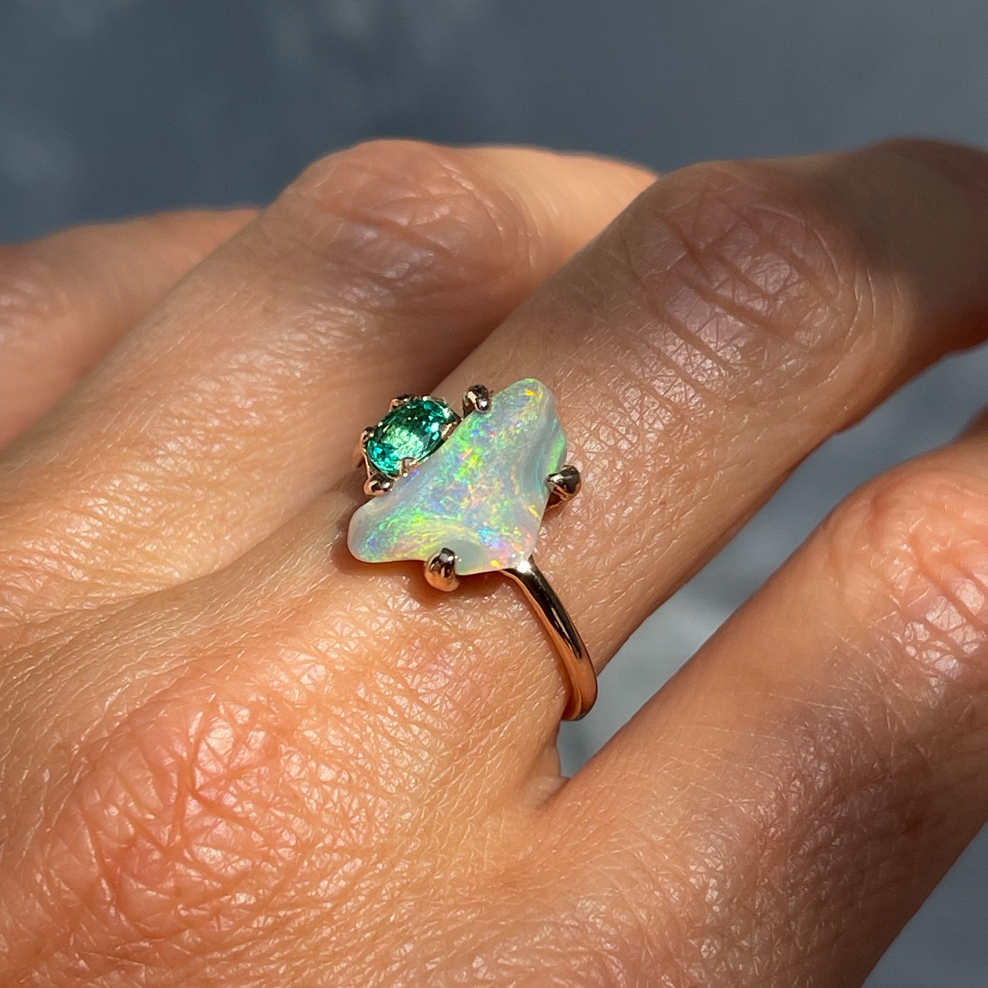 Angled view of an Opal and Emerald Ring by NIXIN Jewelry modeled on the hand. The emerald and Black Opal stone are set in a handmade rose gold ring.