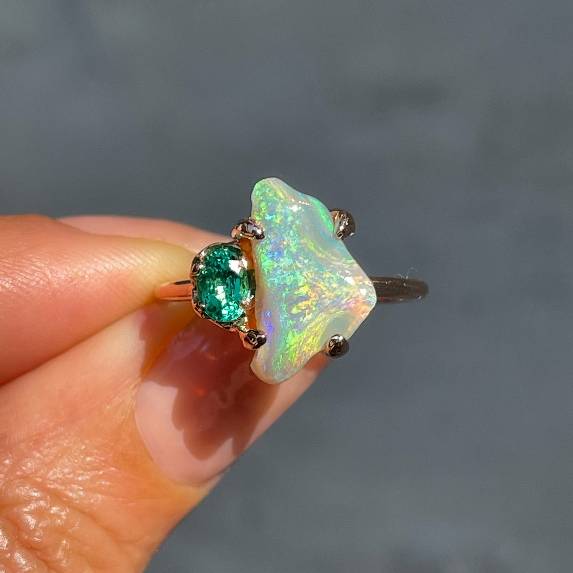An Opal and Emerald Ring by NIXIN Jewelry held in sunlight. The Australian Opal ring is made in 14k rose gold.