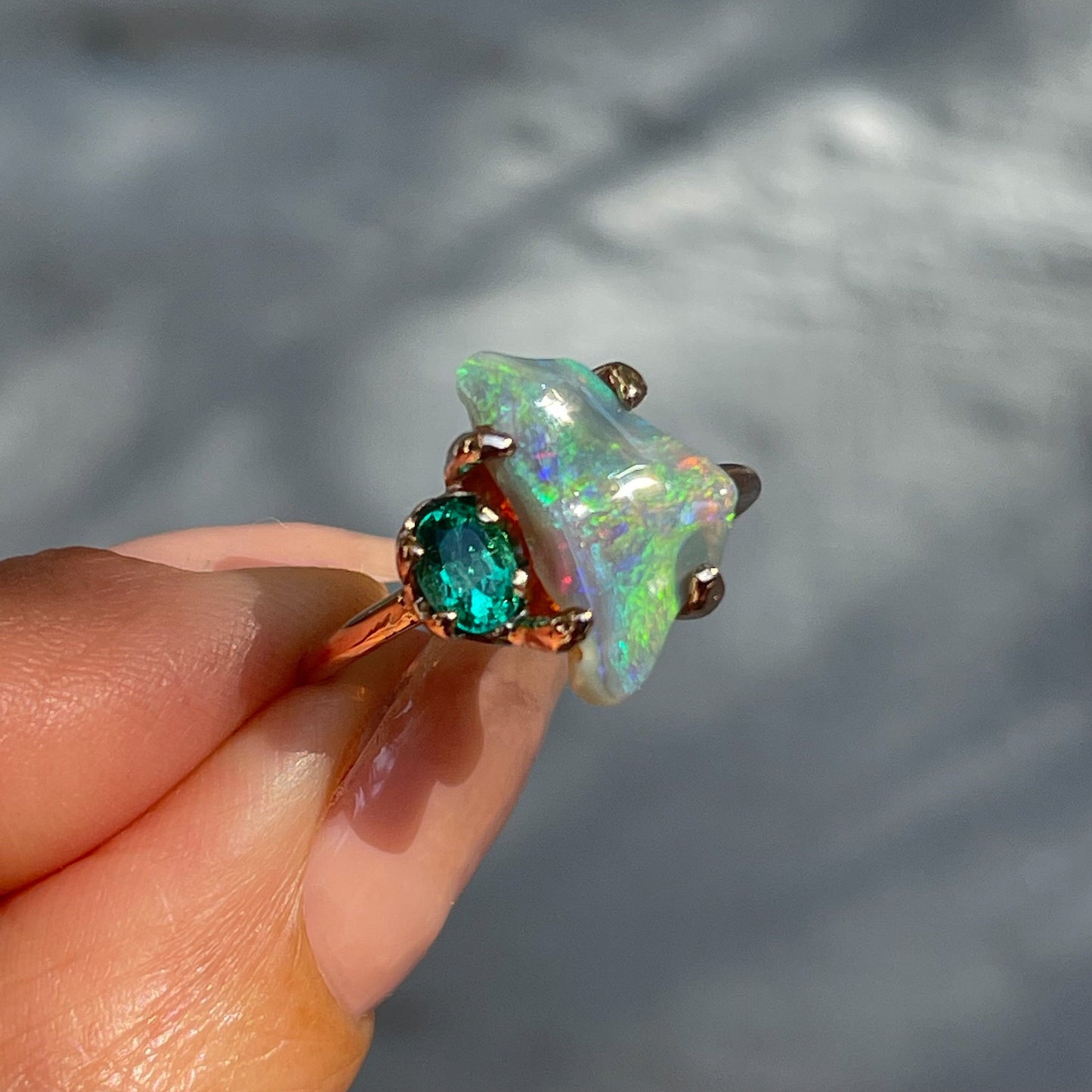 An Opal and Emerald Ring by NIXIN Jewelry shot in partial shade to show the tones of the semi-black opal. A one of a kind opal ring.