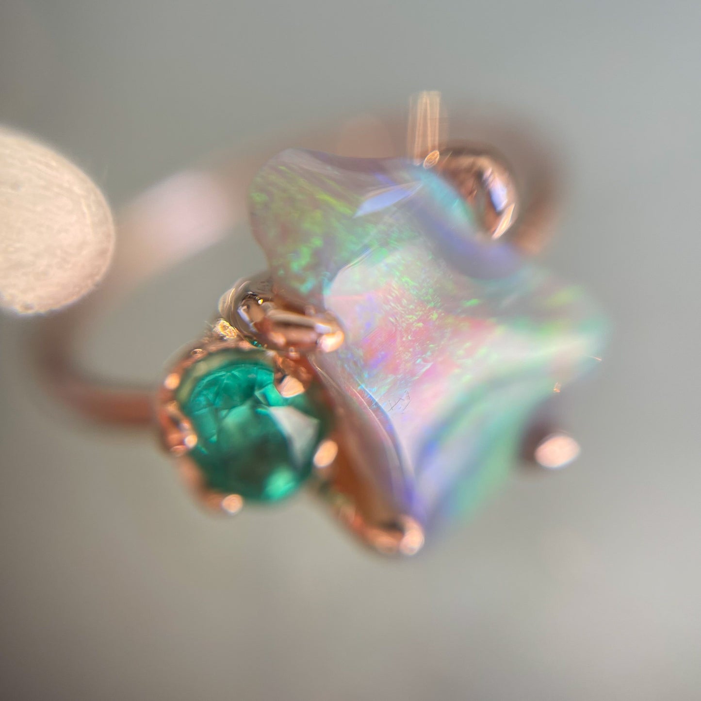 A magnified image of an Opal and Emerald Ring by NIXIN Jewelry, shot from above and in the shade. Photo shows the undulating color pattern in the Australian Opal and the saturation of the green emerald. 