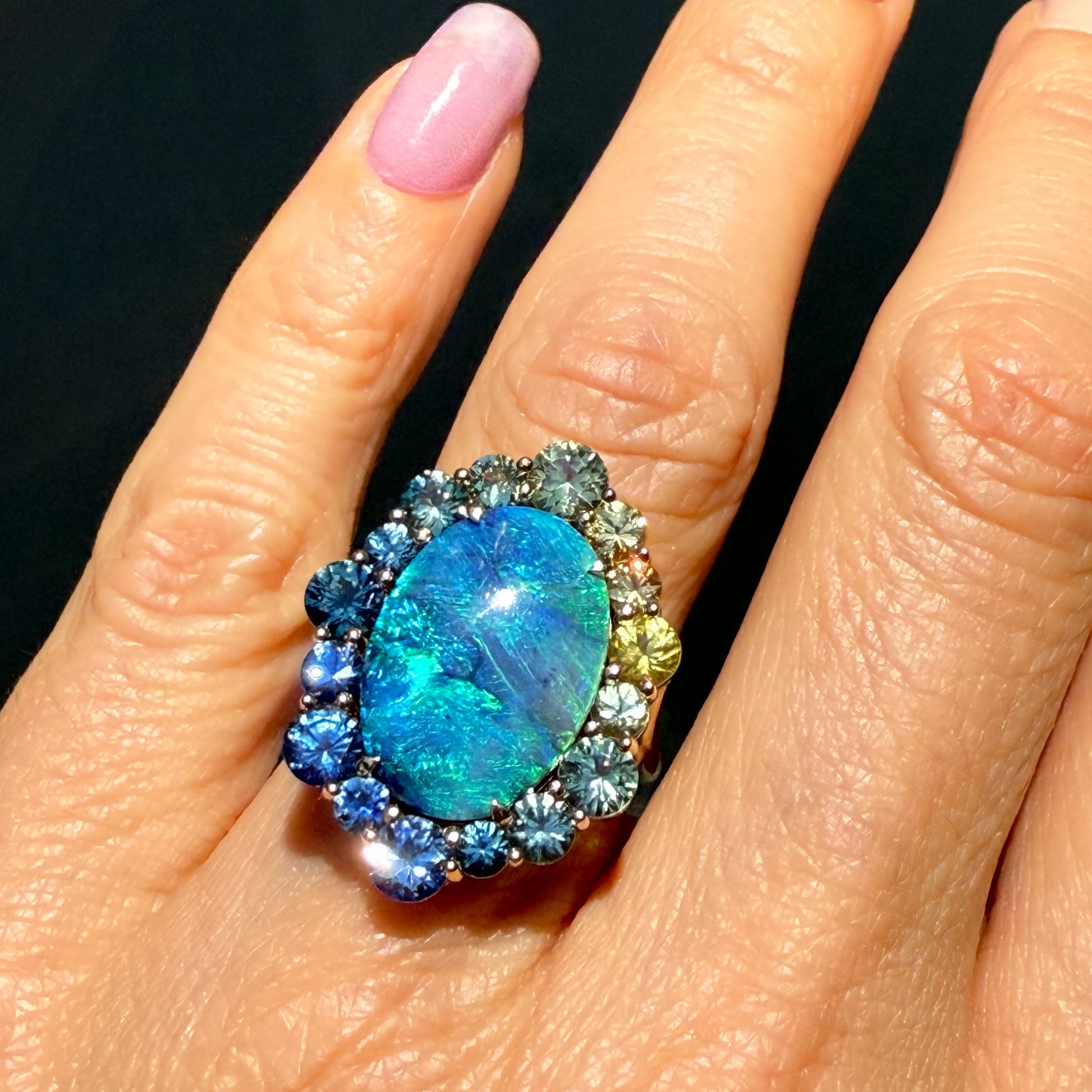 An Australian Opal Ring by NIXIN Jewelry. This sapphire opal ring features a central black opal with feathery fire. It is a rare jewelry piece that is perfect for special occasions.