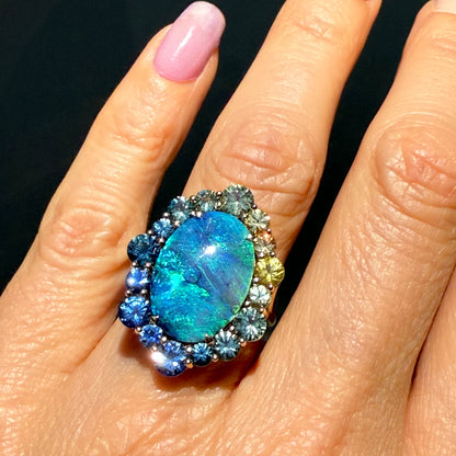 An Australian Opal Ring by NIXIN Jewelry. This sapphire opal ring features a central black opal with feathery fire. It is a rare jewelry piece that is perfect for special occasions.