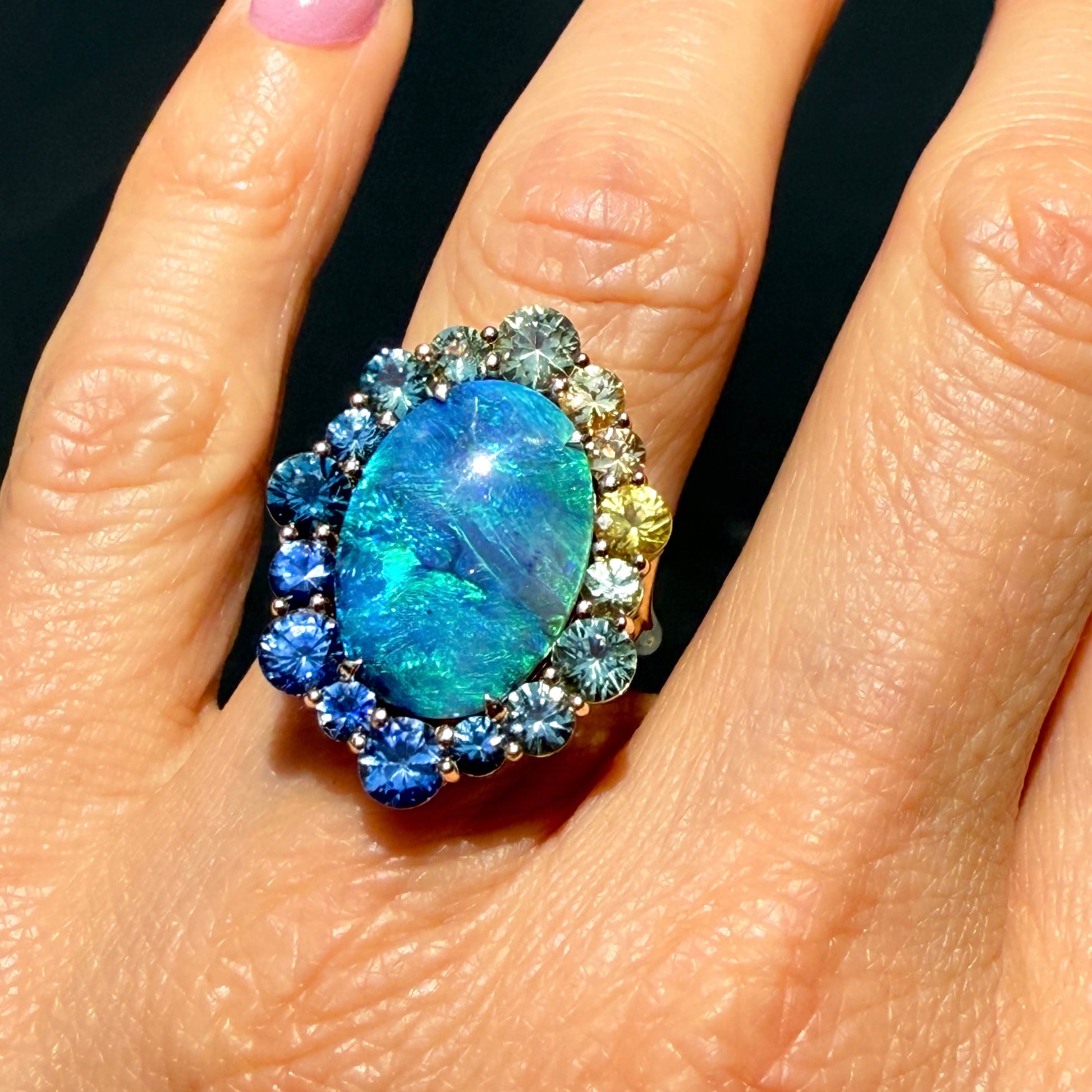 An Australian Opal Ring by NIXIN Jewelry. modeled on a hand. This black opal ring is a spectacular piece of rare jewelry. The natural opal is complemented by a gradient of colorful sapphires.