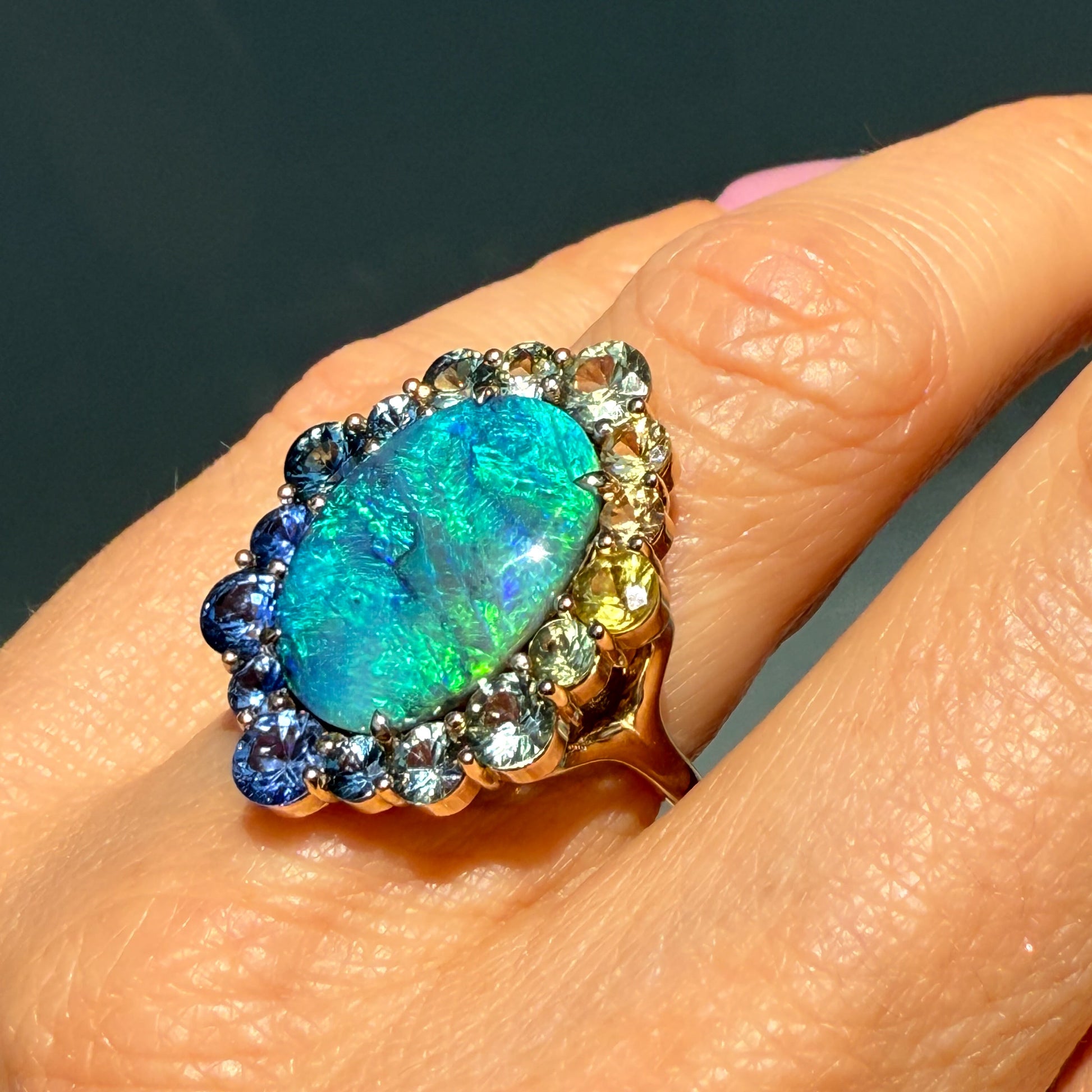 An Australian Opal Ring by NIXIN Jewelry modeled on a hand. This rare opal jewelry piece features an oval-shaped Lightning Ridge Black Opal. The sapphire halo is set in a delicate prong setting.