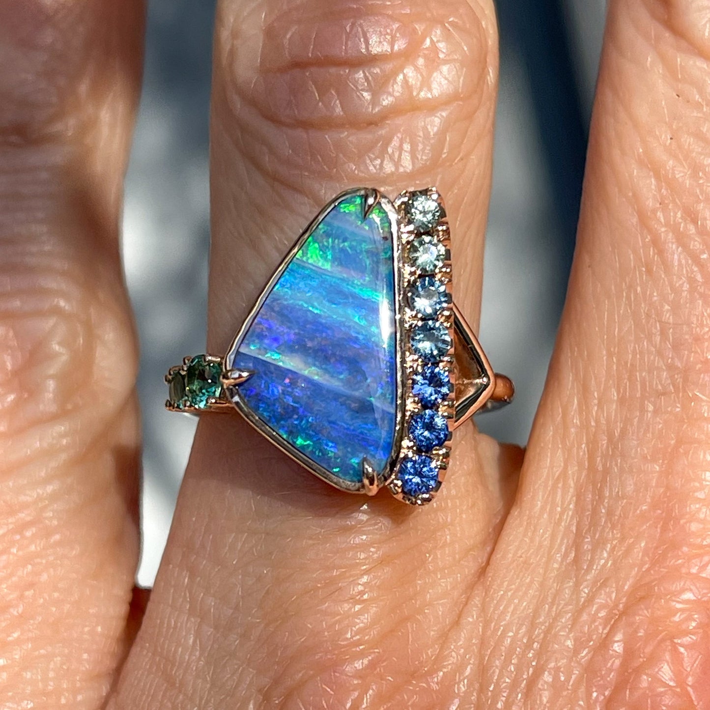 An Australian Opal Ring by NIXIN Jewelry with opal and sapphires modeled on a finger.