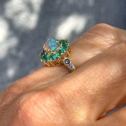 An Australian Opal Ring by NIXIN Jewelry shown in profile. The crystal opal is surrounded by emeralds and sapphires.