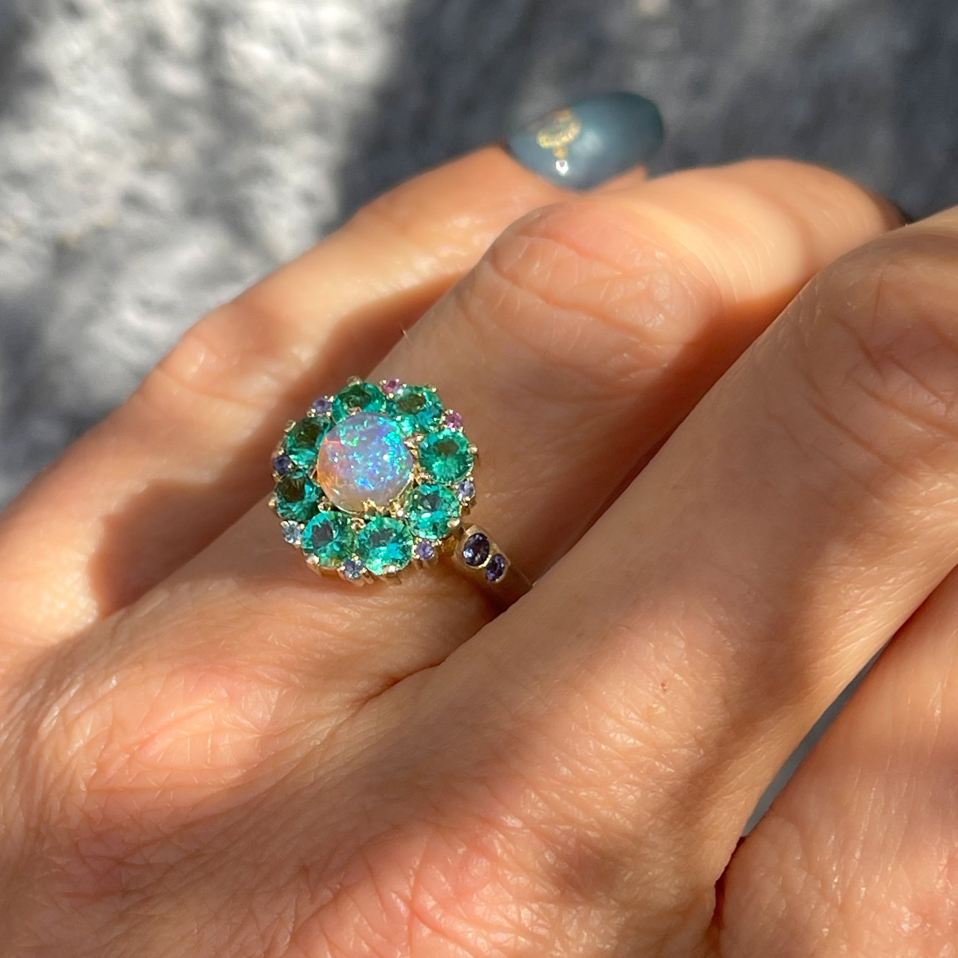 An Australian Opal Ring by NIXIN Jewelry modeled on the hand. A crystal opal ring with an emerald halo.