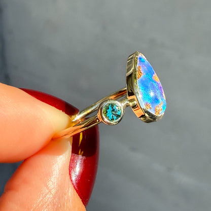 A side profile shot of an Australian Opal Ring by NIXIN Jewelry. The image clearly shows the emerald in its bezel setting, the polished yellow gold band, and the height of the two distinct bezel settings. This dynamic angle showcases the refined nature and modern design of this women's luxury ring.