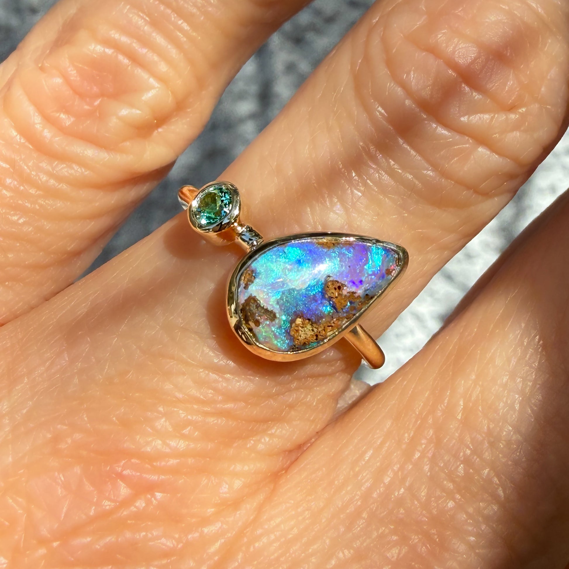 This is an Australian Opal Ring by NIXIN Jewelry showing the unique details of the stone. This macro photograph provides a close-up view of the natural opal in this emerald opal ring, focusing on the complex pattern of the matrix within the blue opal. This distinct pattern showcases the artistry found in rare jewelry and one-of-a-kind opal stones.